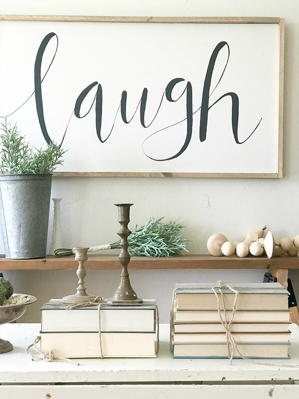 Farmhouse living room ideas complete with large farmhouse signs, pottery, rustic wood, and fresh lilac cuttings. A touch of navy blue accents finishes off the space.