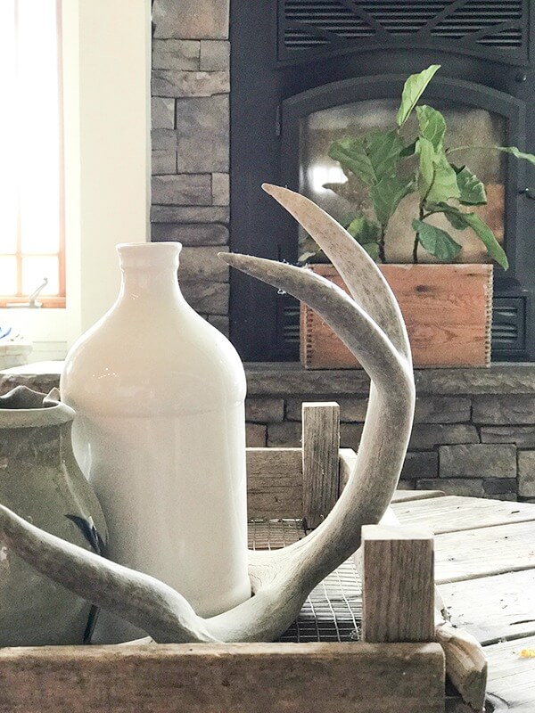 Farmhouse living room summer decor complete with large farmhouse signs, pottery, rustic wood, and fresh lilac cuttings. A touch of navy blue accents finishes off the space.
