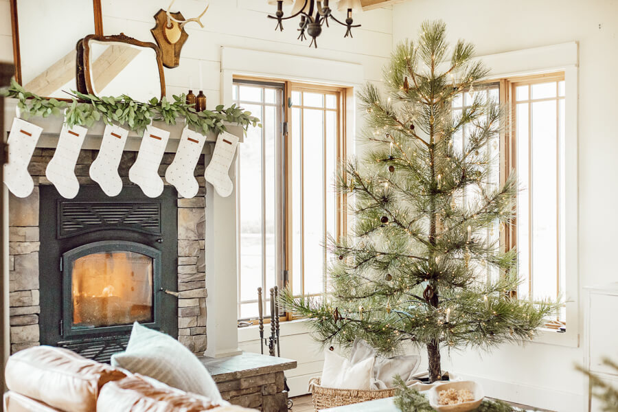 Christmas living room decor including a stacked stone fireplace, antique wood mirrors, deer antlers, a Ponderosa pine tree all decorated for Christmas