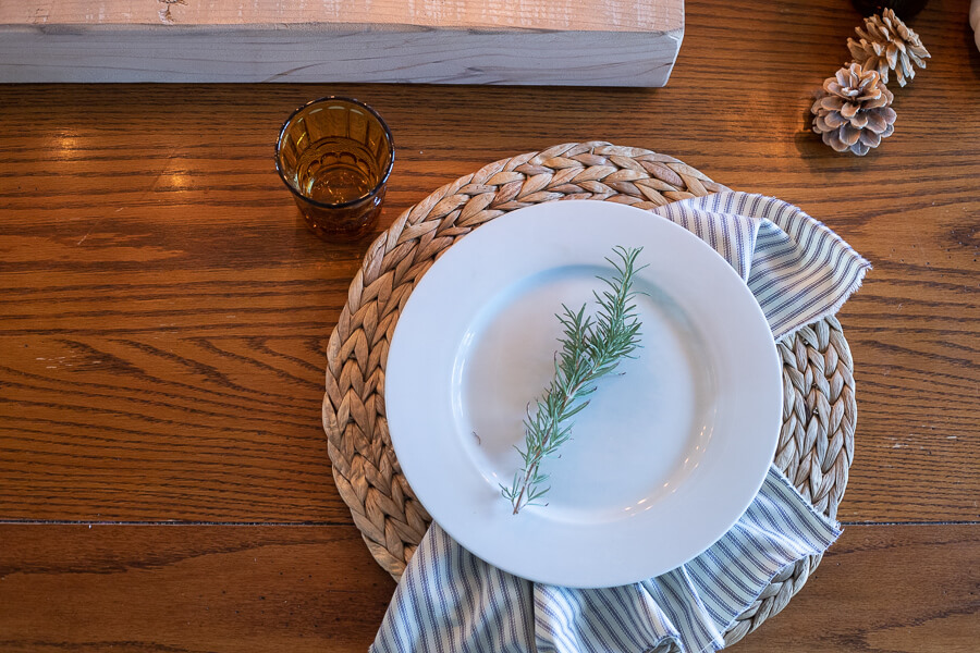 A unique wood candle holder, amber drinking glasses, striped napkins, and simple white dishes create a wonderfully cozy and intimate Thanksgiving tablescape.  Thanksgiving table decor can be simple and inexpensive and still make an impact!