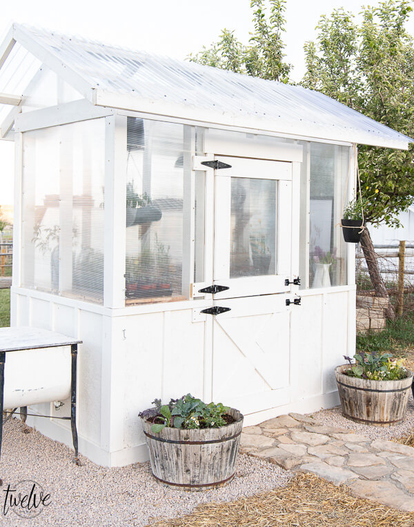 Stylish and functional DIY greenhouse design complete with a dutch door that serves as the window, an outdoor washing station, rustic wood shelving and so much more!