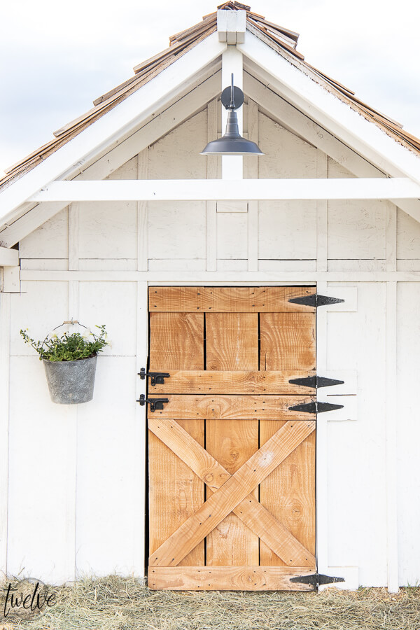 Check out this amazing simple and stylish white and rustic goat house!  Looking for goat shed ideas? We combined function, along with a rustic dutch door, a stylish solar light, rustic shake roof, white board and batten, and so much more to create a simple but stylish goat house! Also includes a gorgeous cupola on the top of the roof!