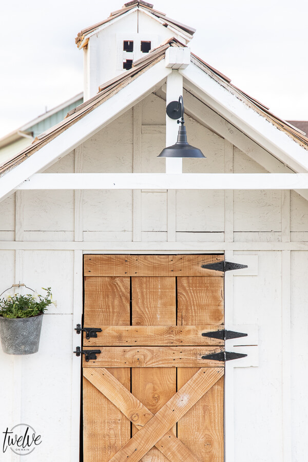 Check out this amazing simple and stylish white and rustic small livestock barn!  Looking for goat shed ideas? We combined function, along with a rustic dutch door, a stylish solar light, rustic shake roof, white board and batten, and so much more to create a simple but stylish goat house!