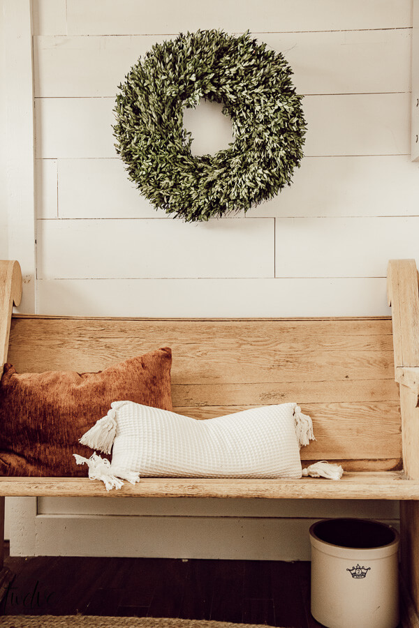 Simple winter decor in the entryway using a festive boxwood wreath and a warm rust colored pillow.