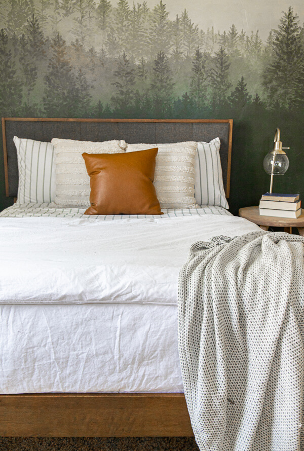 Gorgeous guest bedroom complete with a cozy bed, beautifully painted custom forest wall mural, cozy seating, and so much more.