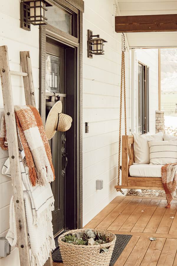 Simple fall front porch decor using items that will bring you from the summer to fall without spending a lot of money! An old ladder serves as a blanket ladder, a hat as a wreath, take advantage of thee falling leaves and use them in your porch decor.